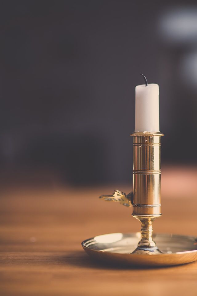 A white candle in a brass holder on a wooden table
